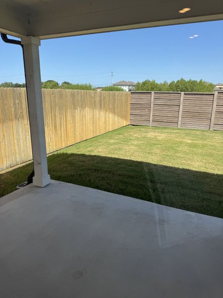 A cozy patio overlooking a fenced backyard with lush grass, perfect for relaxation and outdoor gatherings.