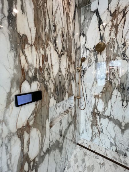 Luxurious shower featuring elegant marble walls, gold fixtures, and a sleek modern control panel.