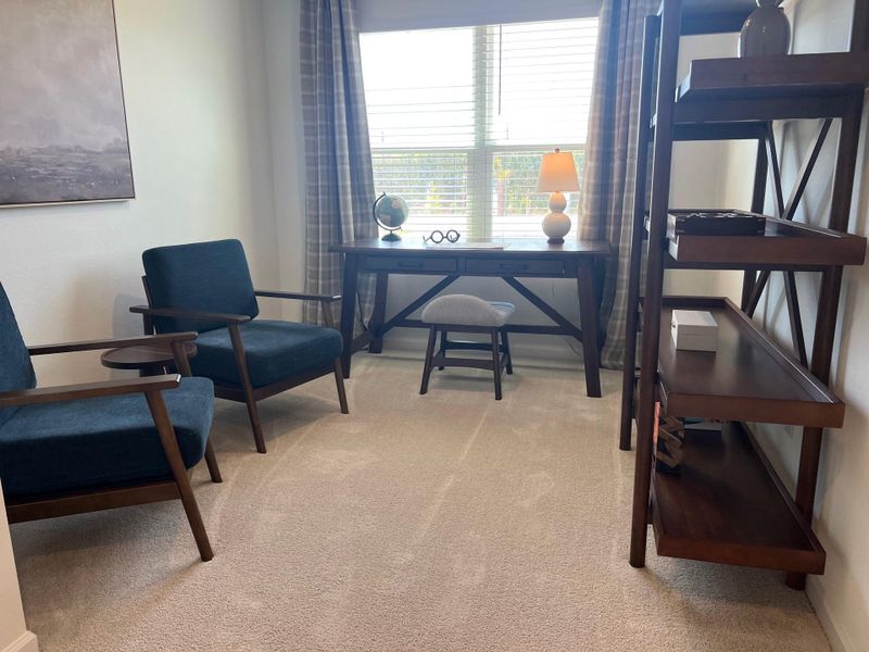 A cozy study with teal chairs, wooden shelves, and a desk by a window, offering a tranquil workspace ambiance.