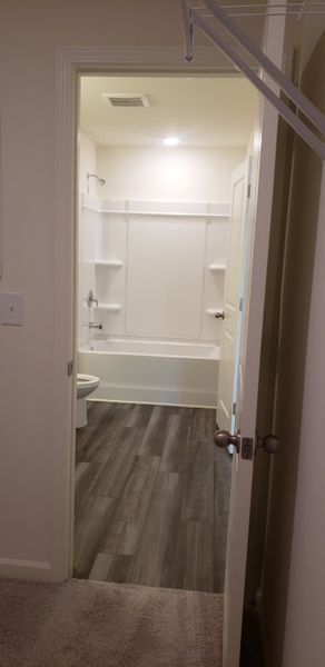 A simple bathroom with a white tub, wood-patterned flooring, and soft carpeted entrance. A simple bathroom with a white tub, wood-patterned flooring, and soft carpeted entrance.
