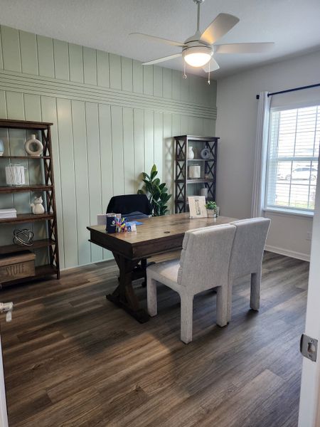 A cozy home office with wood floors, a rustic desk, plush chairs, and a soft green accent wall.