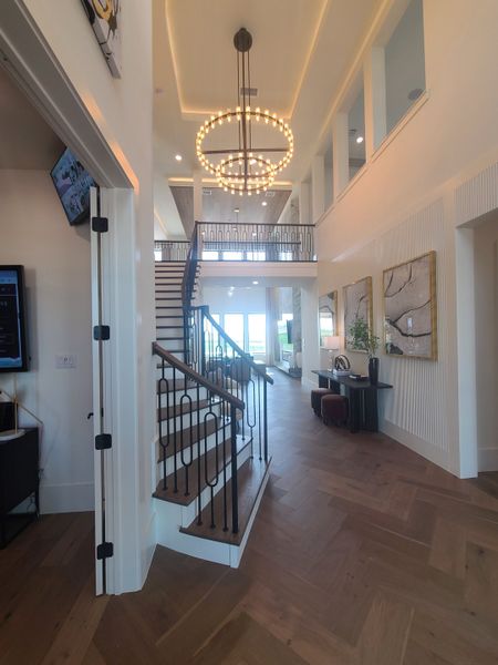 A luxurious foyer with a grand staircase, hardwood floors, and modern chandeliers, exuding elegance and warmth.