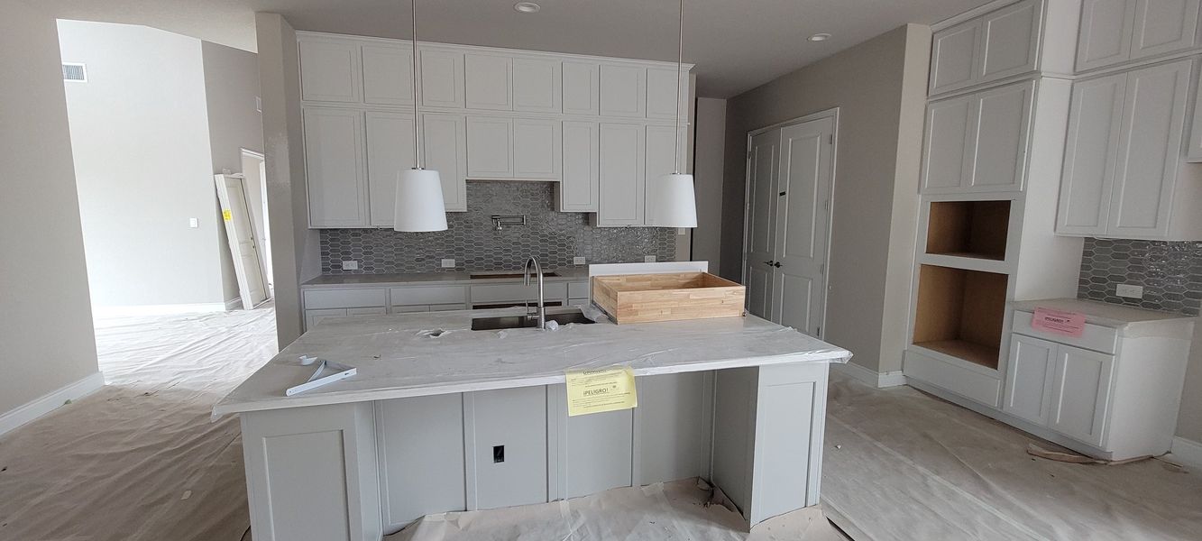 A modern kitchen with white cabinets, a large island, and hexagonal tile backsplash, featuring pendant lights.