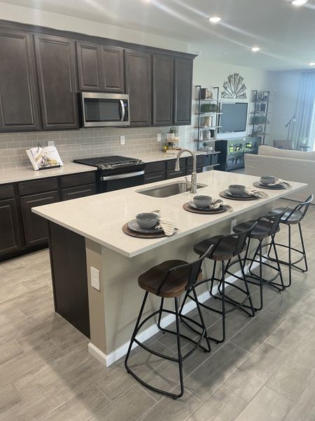 A modern kitchen featuring dark cabinetry, sleek countertops, and a cozy breakfast bar with stylish stools.