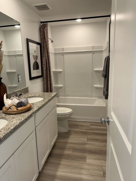 A modern bathroom featuring granite countertops, double sinks, sleek fixtures, and warm wood flooring. A modern bathroom featuring granite countertops, double sinks, sleek fixtures, and warm wood flooring.