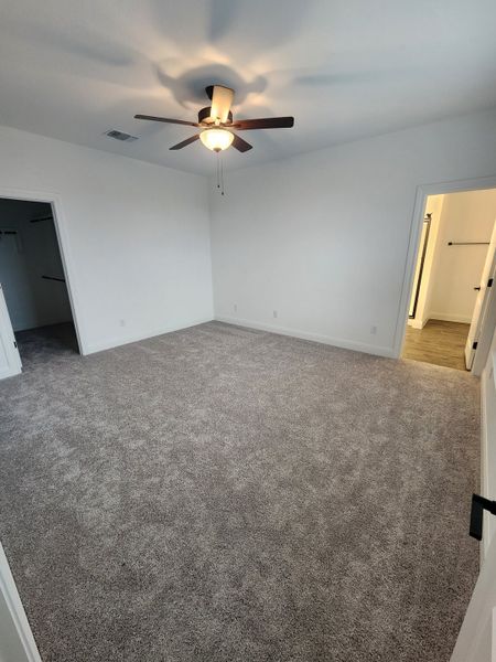 A spacious bedroom with plush carpet, ceiling fan, and modern closet space.