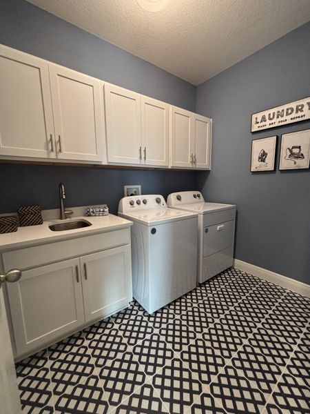 A laundry room with bold patterned tile flooring, white cabinetry, and ample storage space in Crossroads at Kelly Park by Dream Finders Homes (Apopka, FL).