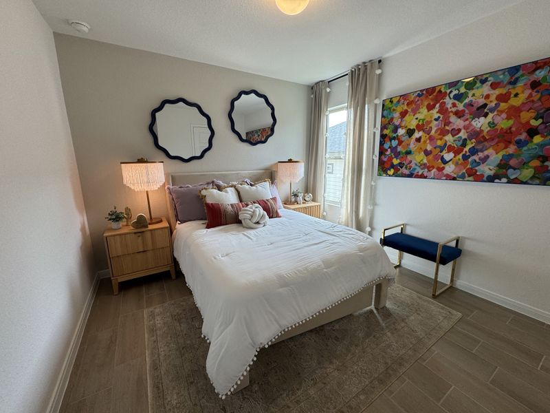 A cozy bedroom featuring a plush bed with layered pillows, elegant mirrors, framed heart artwork, and soft lighting.