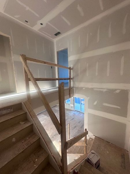 A staircase under construction with wooden railings and drywall, allowing a glimpse into a future modern home.