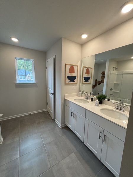 A spacious bathroom featuring a dual-sink vanity, sleek tile flooring, and contemporary artwork.