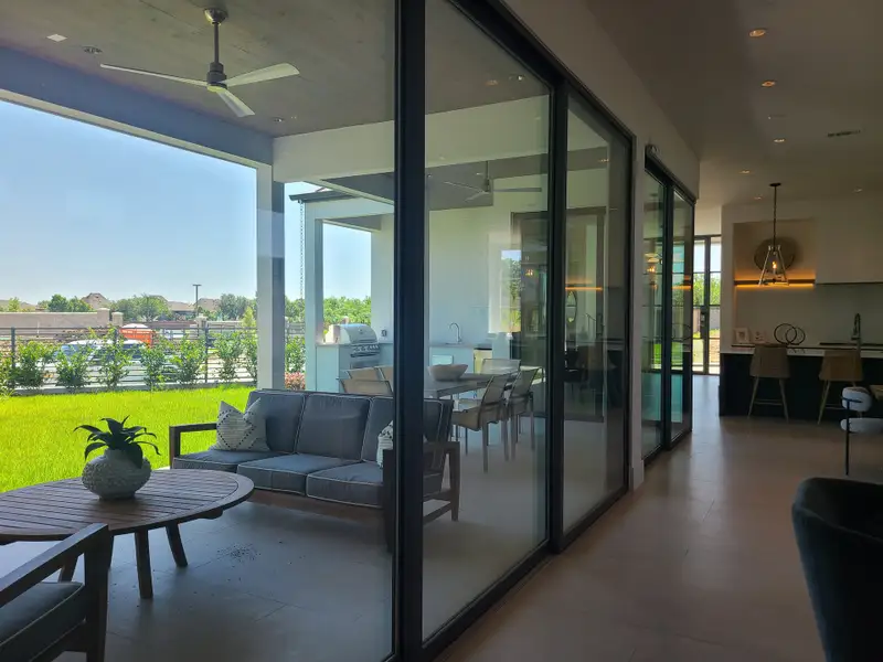 A spacious patio with modern furniture, expansive glass doors, and a view of a lush green garden, perfect for relaxation.