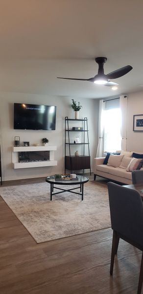 A modern living room with a wall-mounted TV, sleek shelves, cozy sofa, and contemporary fan. Neutral tones and elegant decor. A modern living room with a wall-mounted TV, sleek shelves, cozy sofa, and contemporary fan. Neutral tones and elegant decor.