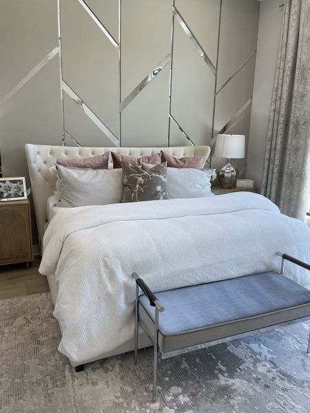 A luxurious bedroom featuring a tufted headboard, elegant geometric accent wall, and plush seating bench in soothing neutral tones.