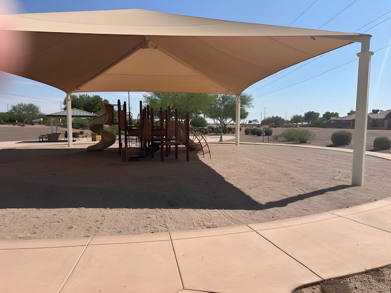A shaded playground with a slide in Magnolia at Desert Passage by KB Home, providing a fun outdoor space in Maricopa, AZ.