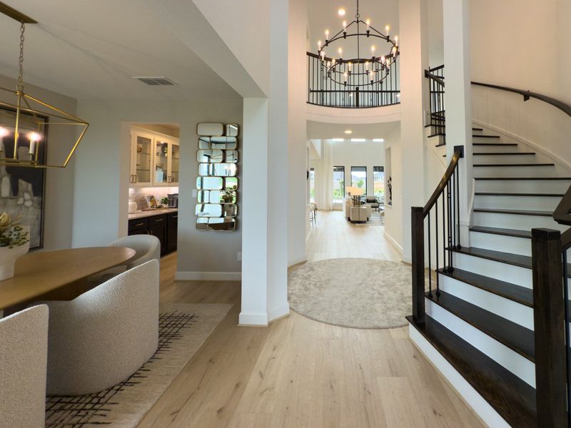 A welcoming foyer with elegant chandelier, curved staircase, and modern dining area leading to a bright open living space. A welcoming foyer with elegant chandelier, curved staircase, and modern dining area leading to a bright open living space.
