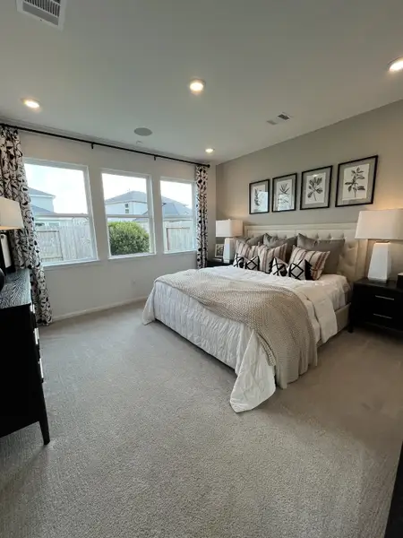 A cozy bedroom featuring a plush bed, soft carpeting, and large windows with elegant curtains and framed botanical artwork. A cozy bedroom featuring a plush bed, soft carpeting, and large windows with elegant curtains and framed botanical artwork.