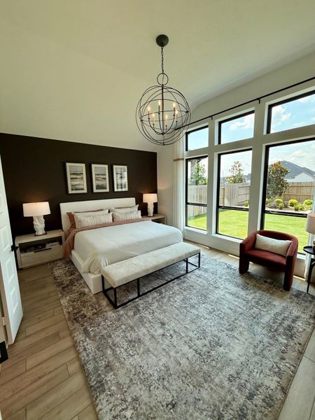 A cozy bedroom with large windows, an elegant chandelier, and a soft area rug.