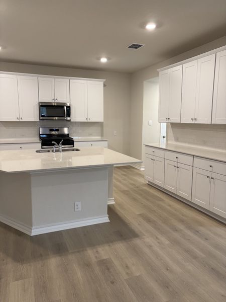 A modern kitchen with sleek white cabinets, stainless steel appliances, and warm wood flooring.