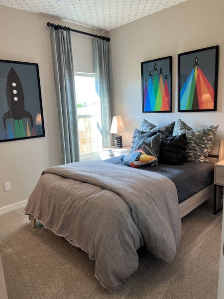 A cozy bedroom featuring space-themed artwork and modern gray decor, complete with plush bedding and soft carpeting.