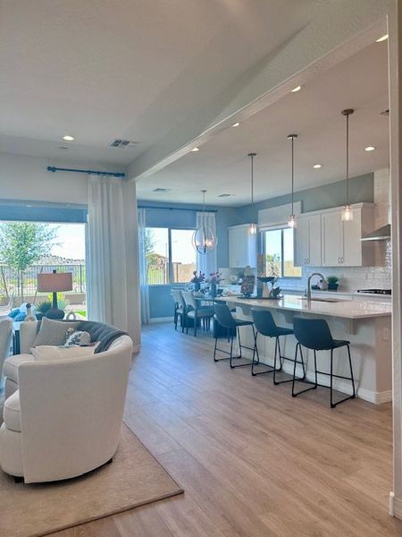 An open-concept living area with sleek kitchen, island seating, and bright dining space under elegant pendant lighting.