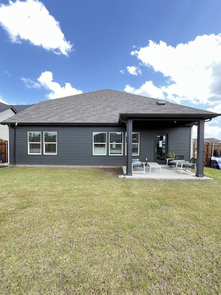 A beautiful gray home with a spacious yard and covered patio in Tesoro at Chisholm Trail Ranch by Meritage Homes (Crowley, TX).