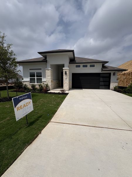 A modern home with stone accents and a sleek garage in Veranda by Brightland Homes (San Antonio, TX).