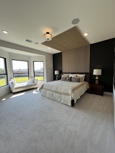 A spacious bedroom featuring a cozy bed, accent wall, and a sunlit sitting area by large windows.