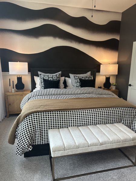 A modern bedroom featuring bold, artistic wall art, a patterned bedspread, and a cozy upholstered bench. A modern bedroom featuring bold, artistic wall art, a patterned bedspread, and a cozy upholstered bench.