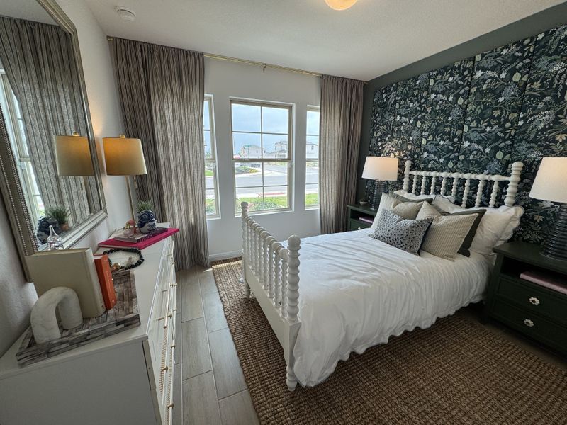 A cozy bedroom with floral accent wall, spindle bed, and elegant lighting, complemented by a woven rug and stylish dresser.