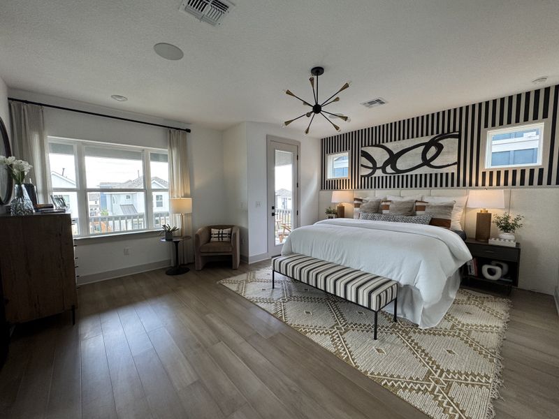 A modern bedroom with striped accents, a cozy bench, large windows, and stylish lighting.