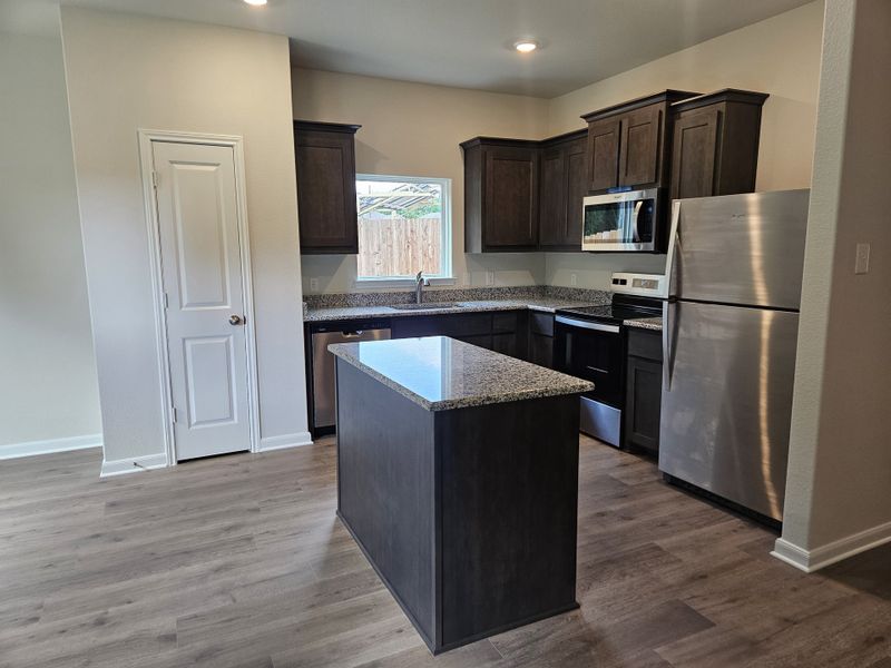A modern kitchen with granite countertops, dark wood cabinets, and stainless steel appliances.