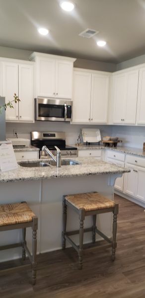 A modern kitchen with white cabinetry, granite countertops, island seating, and stainless steel appliances.