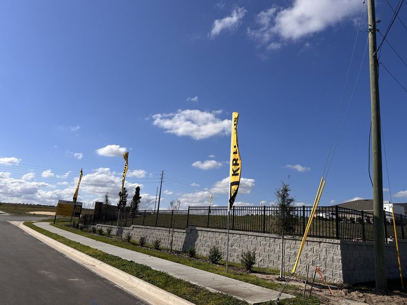 An entrance to the KB Home community, lined with yellow flags and a clear blue sky in Landings at Lake Mabel Loop by KB Home (Dundee, FL).