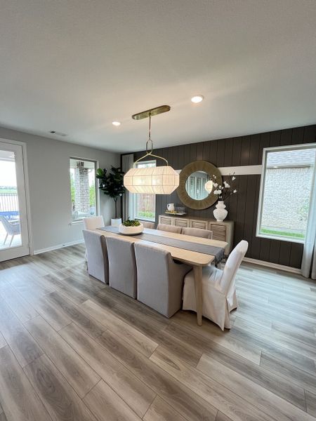 A sleek dining area with a modern chandelier, wood flooring, and large windows creating a bright, airy atmosphere.
