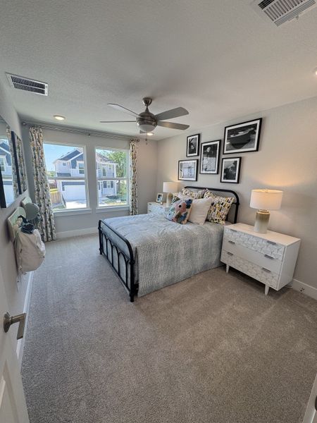 A cozy bedroom with a stylish metal bed, modern decor, large window, and plush carpeting, offering a serene retreat.