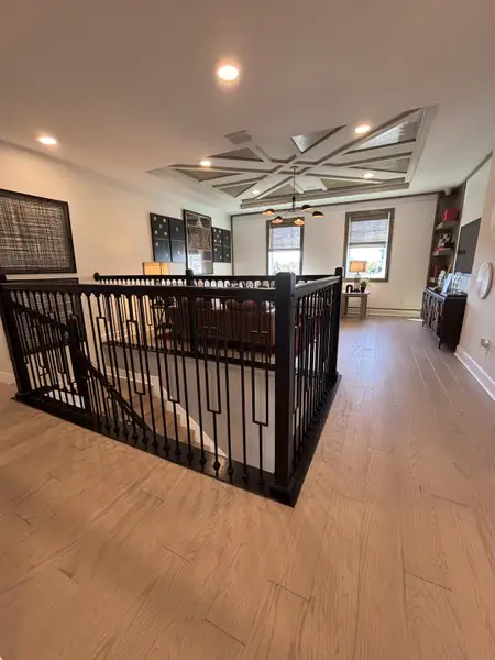 A stylish loft area with intricate ceiling details, wood flooring, and sleek railing in Eden at Crossprairie by M/I Homes (St. Cloud, FL).