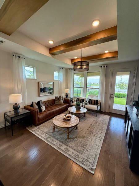 A cozy living room featuring a leather sofa, rustic coffee tables, wood beam ceiling, and abundant natural light. A cozy living room featuring a leather sofa, rustic coffee tables, wood beam ceiling, and abundant natural light.