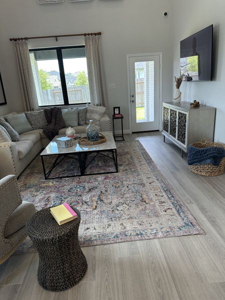 A cozy living room with a large sectional, patterned rug, and stylish decor, featuring a bright window and hardwood floor. A cozy living room with a large sectional, patterned rug, and stylish decor, featuring a bright window and hardwood floor.