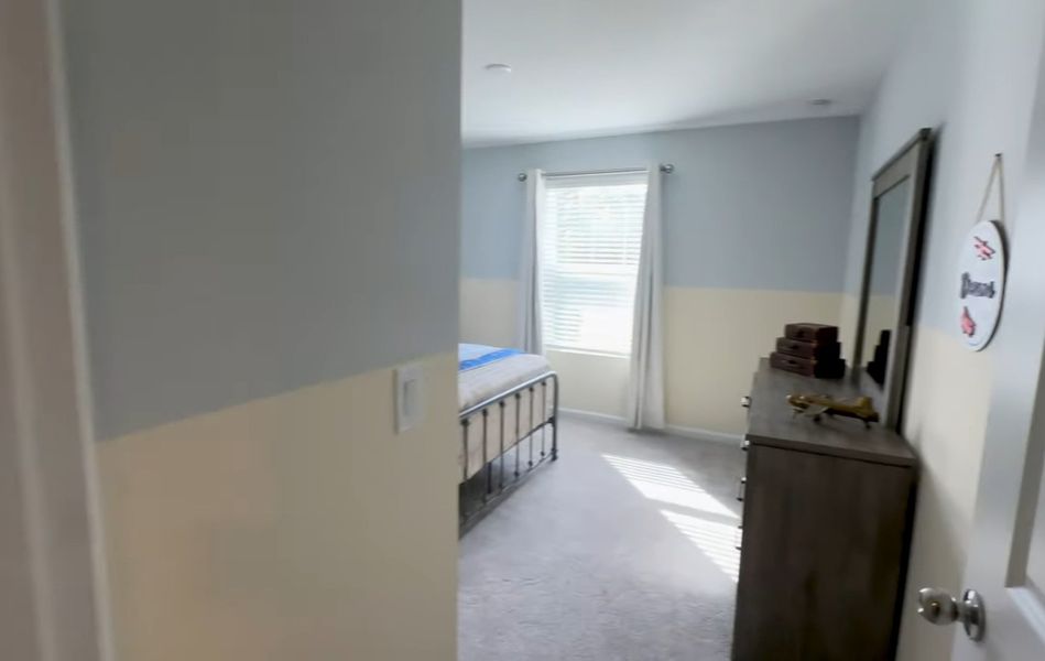 A cozy bedroom with soft, neutral walls, a large window with blinds, and a stylish dresser with decor.