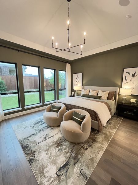 A serene bedroom featuring a modern chandelier, plush seating, and a large window with garden views.