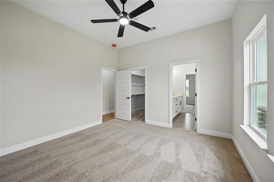 Unfurnished bedroom with light colored carpet, a spacious closet, a ceiling fan, and ensuite bathroom Unfurnished bedroom with light colored carpet, a spacious closet, a ceiling fan, and ensuite bathroom
