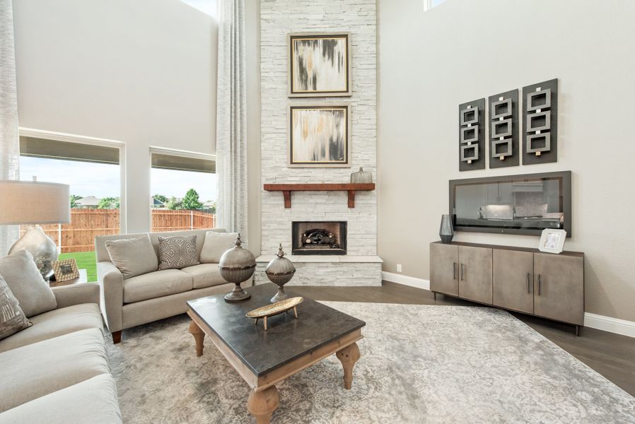 Living room with two-story ceiling, stacked stone fireplace, gray sofas, and large windows with backyard view