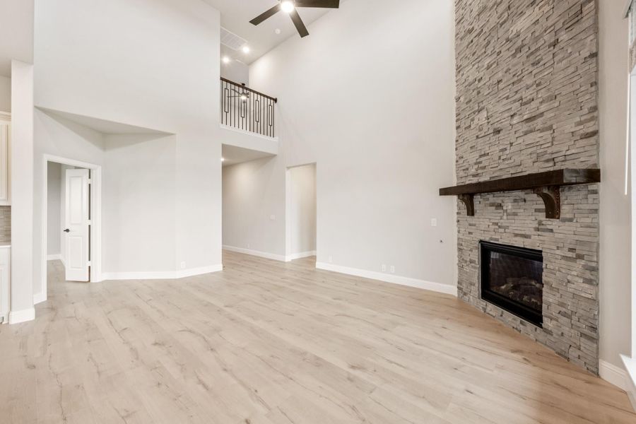 Open living room with vaulted ceiling, stacked stone fireplace, and light hardwood floors