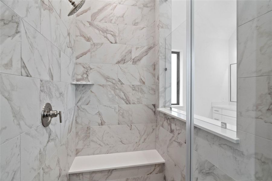 The walk-in shower includes a convenient, integrated bench with a niche shelf, offering comfort, extra storage space, and a high-end, custom appearance.