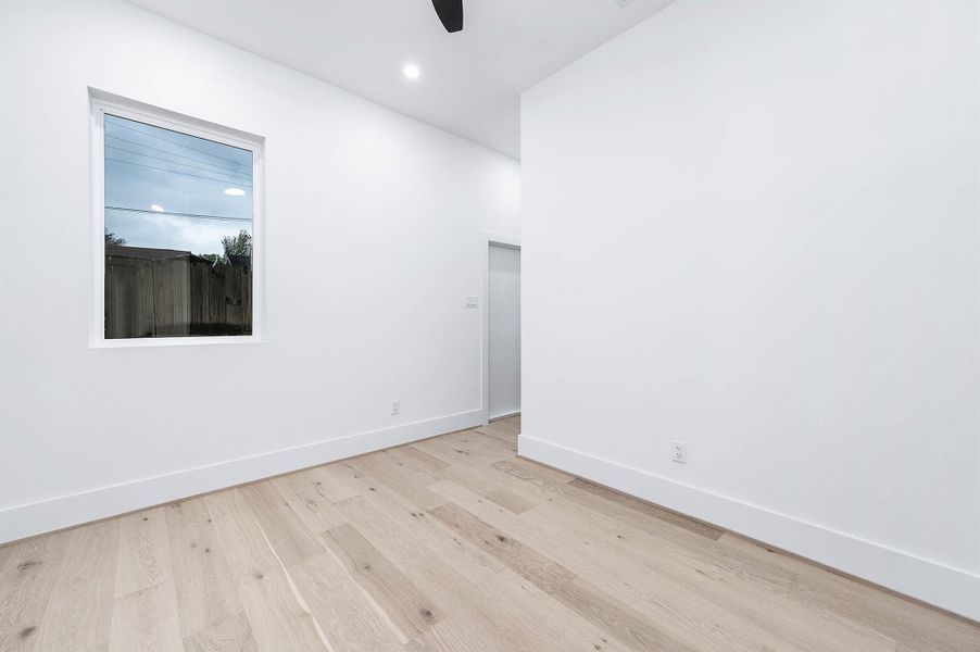 Bright, minimalist room with light wood flooring, white walls, a window providing natural light, and a ceiling fan. Perfect for a modern touch.