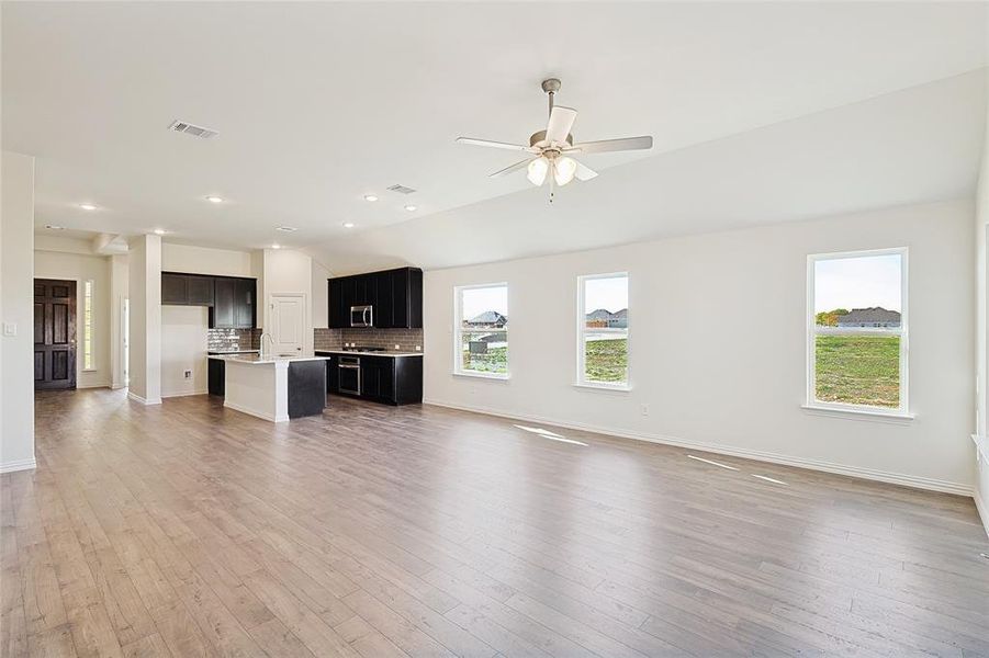 Unfurnished living room featuring a wealth of natural light, hardwood / wood-style floors, ceiling fan, and vaulted ceiling