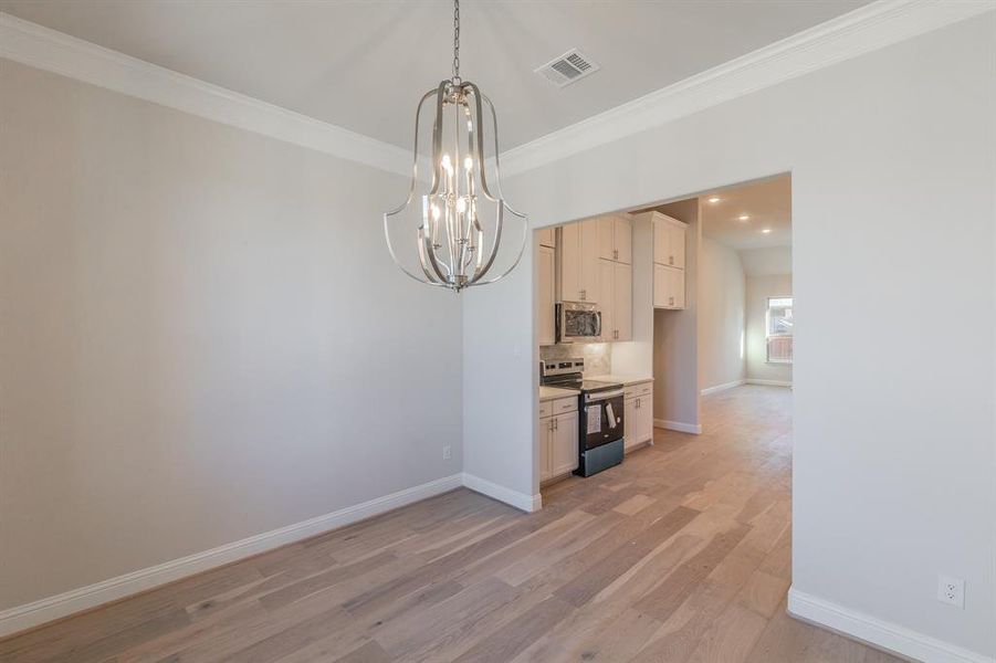 Unfurnished dining area featuring light hardwood / wood-style floors, crown molding, and a chandelier