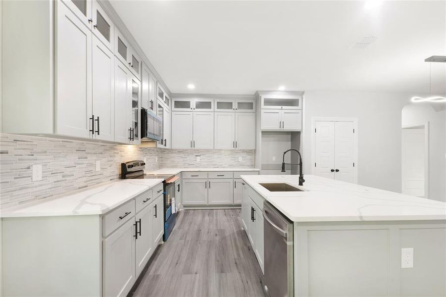 Kitchen featuring light stone counters, range with electric stovetop, an island with sink, light wood finished floors, and white cabinetry