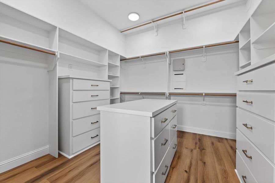 Expansive walk-in closet featuring custom white cabinetry, integrated shelving units, multiple hanging rods, a central storage island with drawers, and wood-finish flooring