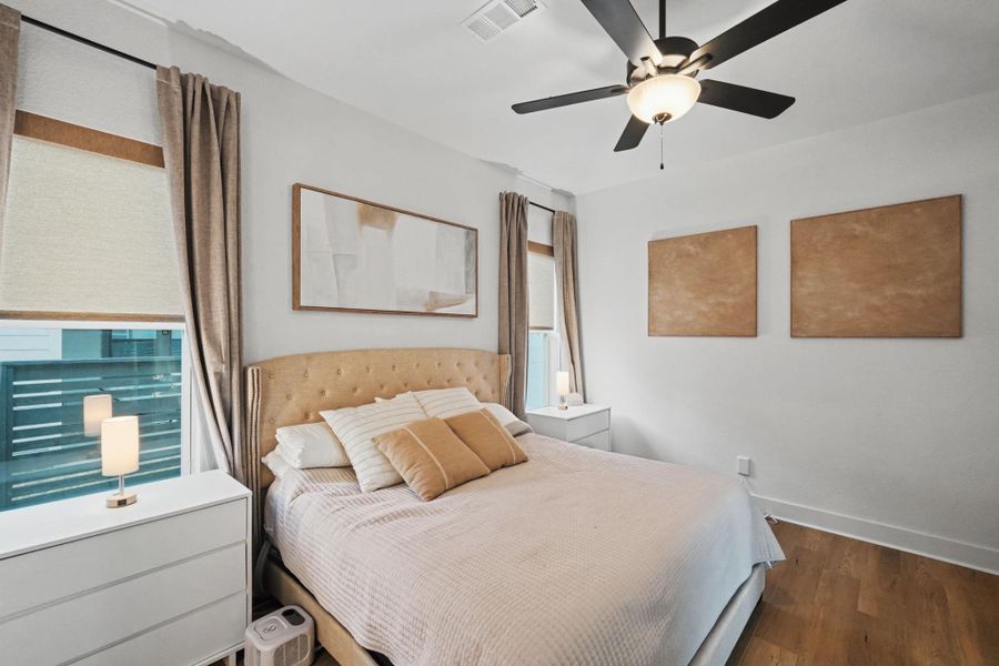 Elegant and inviting bedroom featuring warm wood flooring, soft neutral tones, and abundant natural light. The well-proportioned layout offers a refined retreat with modern finishes and a serene ambiance designed for comfort and relaxation.